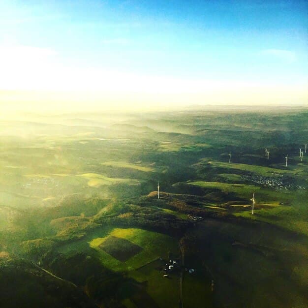 An aerial view of a vast wind farm against a clear blue sky, with lush green fields in the foreground, symbolizing sustainable energy and environmental stewardship.