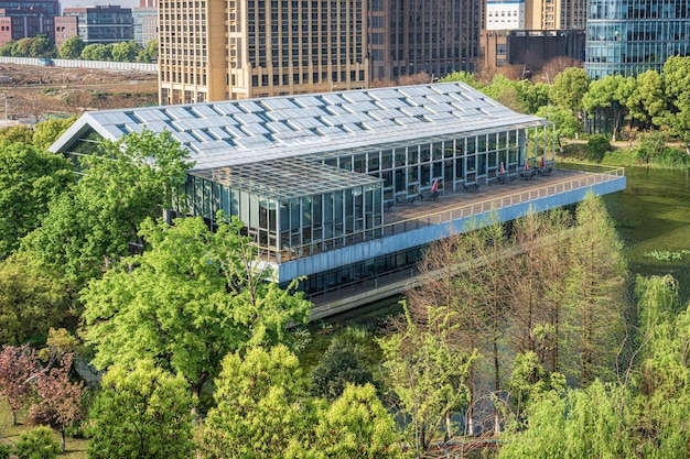 A modern office building with a green roof. Solar panels are integrated into the roof design. The building is surrounded by trees and greenery.