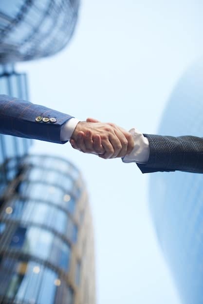 A close up image of two executive hands shaking in front of a skyscraper with a blue sky.